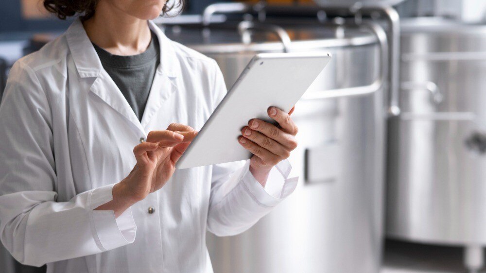 Fotografia de uma mulher mexendo no tablet em uma indústria de alimentos