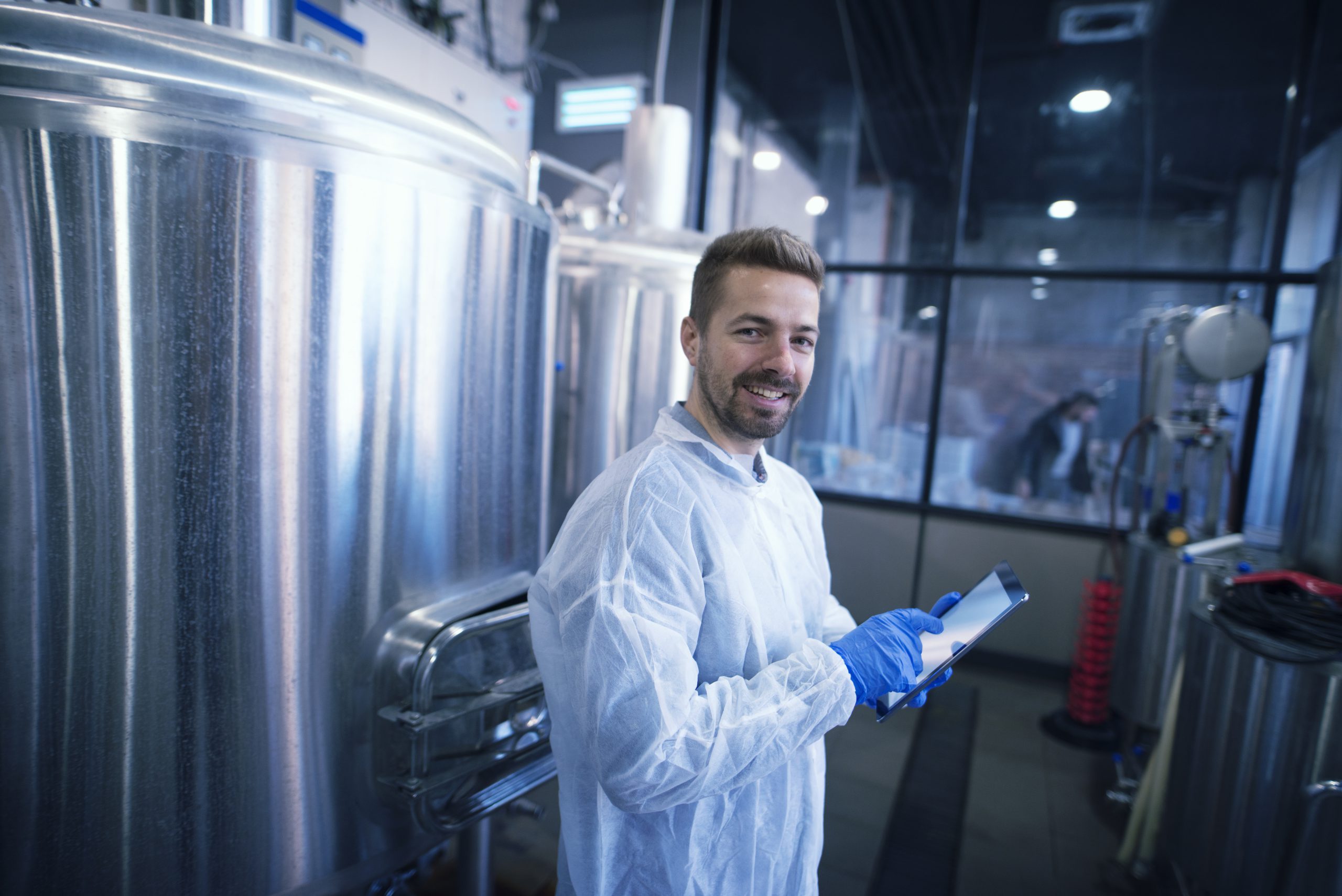 Fotografia de homem branco usando jaleco e luvas sorrindo para a câmera dentro de um laboratório industrial